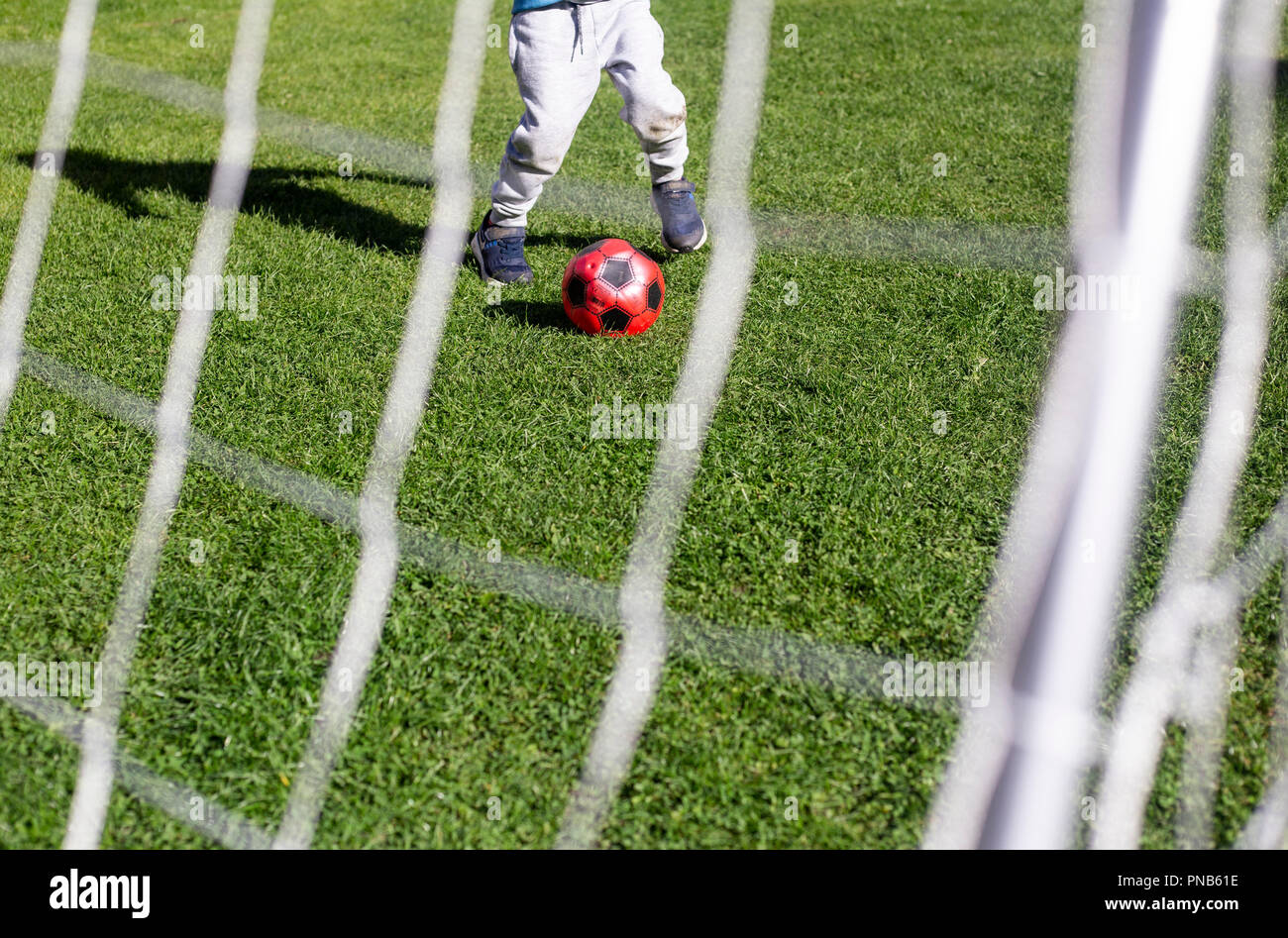 Bambino gioca a calcio in giardino, shot presa attraverso l'obiettivo Foto Stock