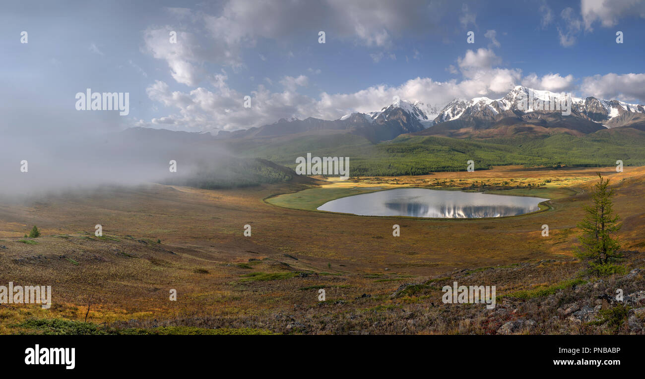 Un fantastico panorama dall'alto su un bellissimo lago, le montagne coperte di neve e foresta, nebbia e nuvole e cielo blu Foto Stock