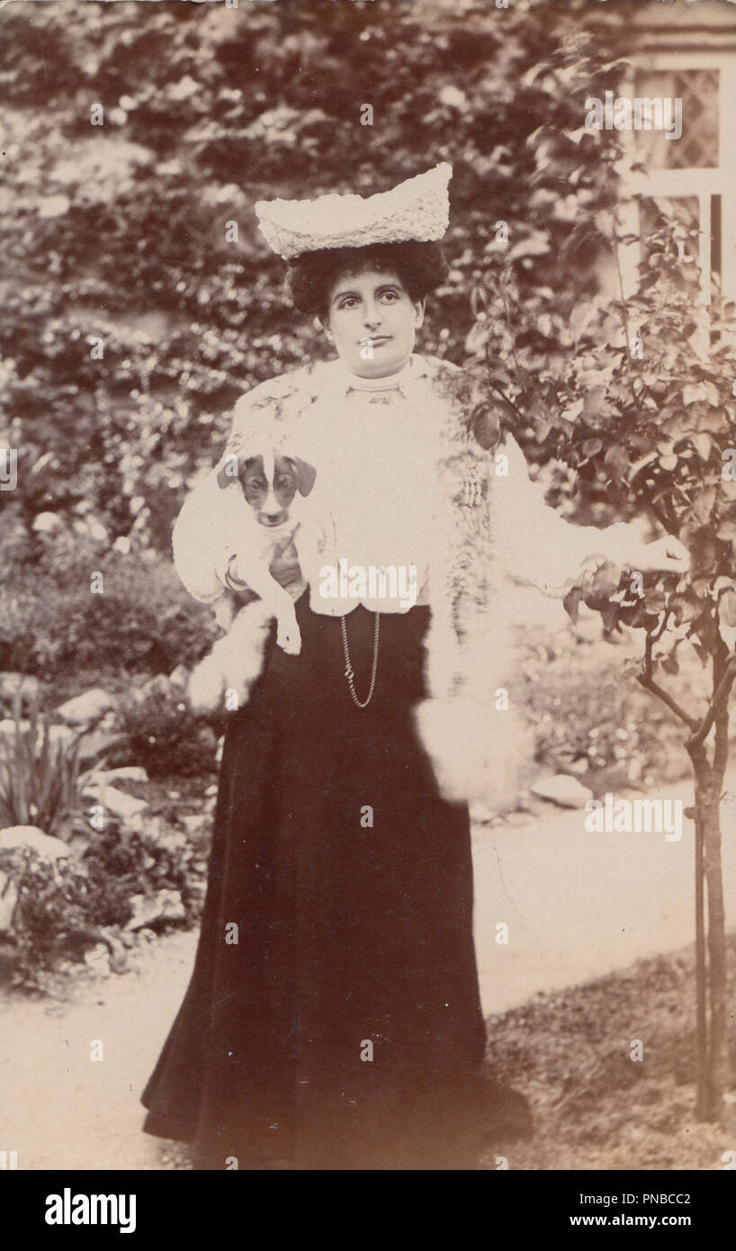 * Vintage fotografia di un elegante Edwardian Lady si fermò nel suo giardino mentre tiene il suo cane Foto Stock
