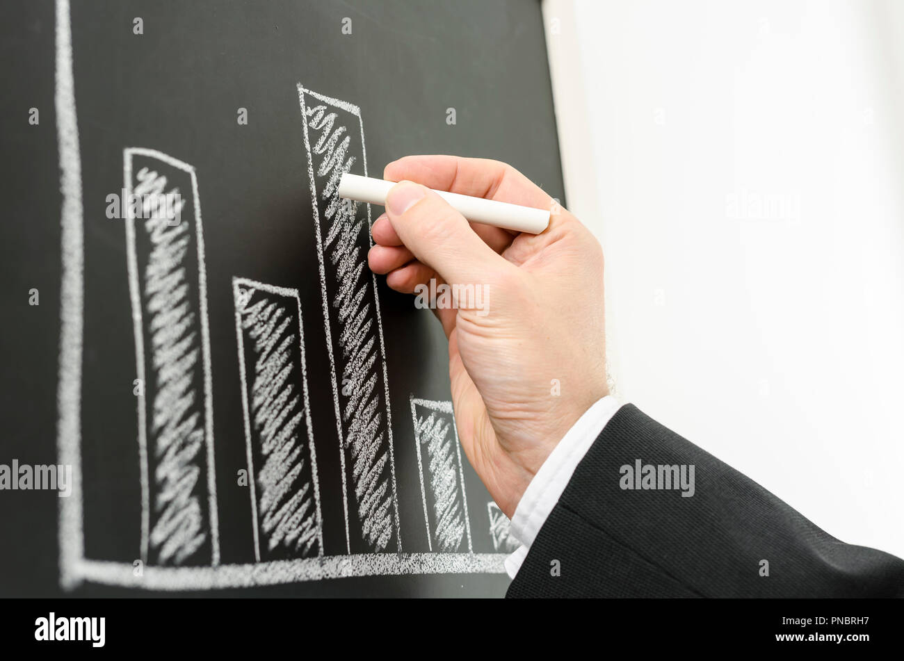 Vista laterale di un imprenditore il canto di disegno grafico di business con un gesso su una lavagna nera. Foto Stock