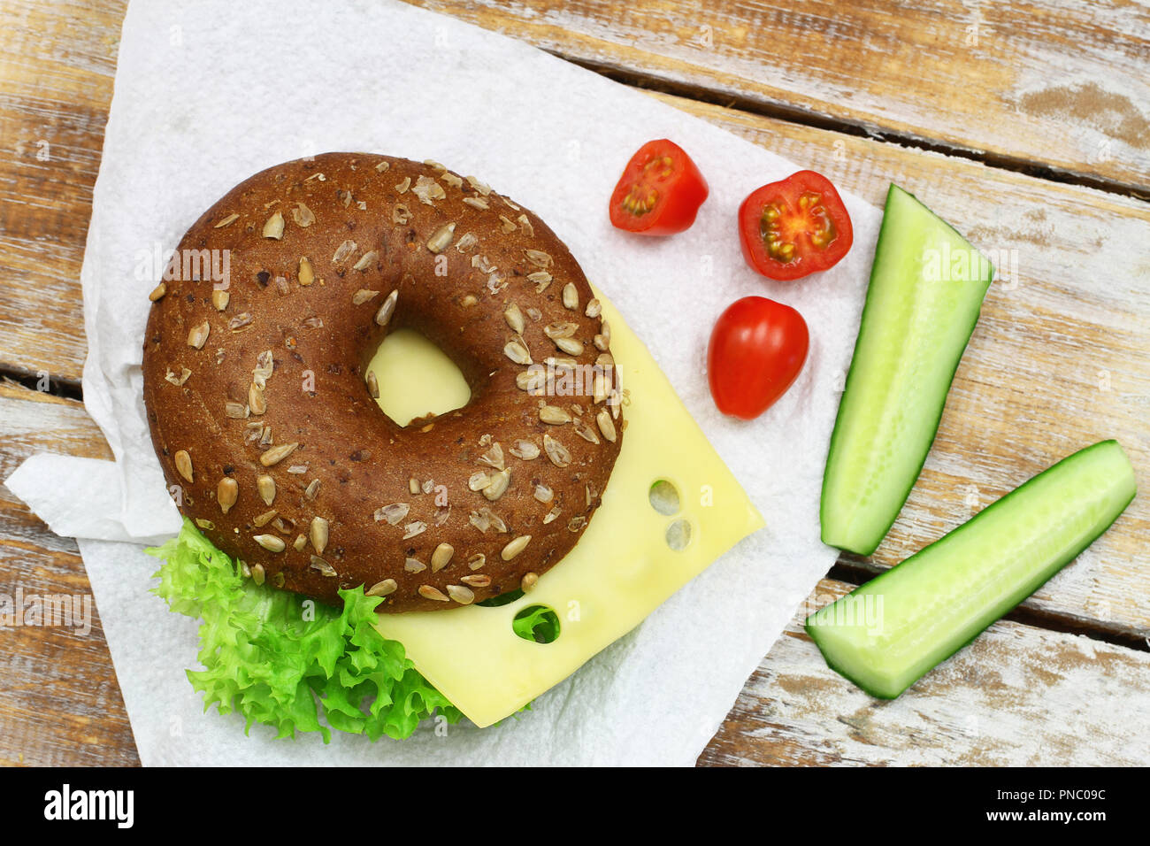 Brown bagel con formaggio e lattuga su carta bianca e i pomodori ciliegia e bastoncini di cetriolo Foto Stock