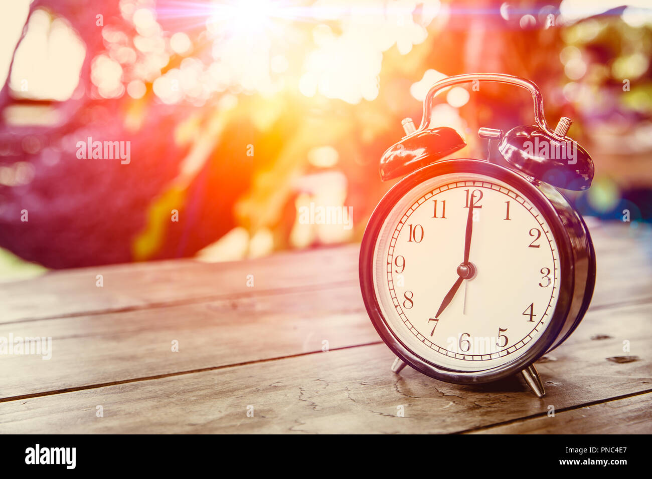 Orologio sul tavolo di legno con effetto di luce del sole di mattina volte a 7 ore. Foto Stock