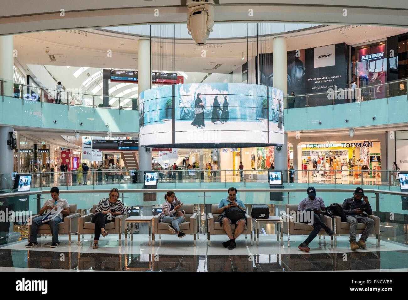 Persone sedute e utilizzando i telefoni cellulari nel centro commerciale di Dubai, Emirati Arabi Uniti, Emirati Arabi Uniti, Foto Stock