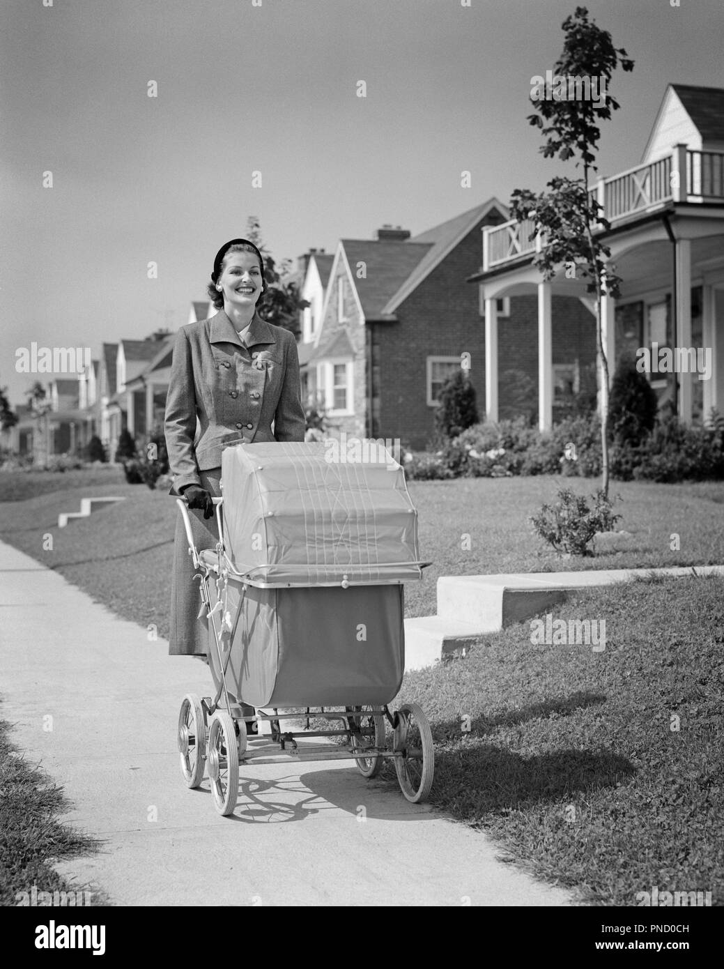 Anni Cinquanta donna sorridente madre camminare spingendo BABY carrello lungo il marciapiede suburbana - b6955 HAR001 HARS FELICITÀ ATTIVITÀ FISICA allegro rafforzare la stima di sé lungo l orgoglio sorrisi SALUTE MENTALE FLESSIBILITÀ DEI MUSCOLI gioiosa elegante baby carrelli MID-adulto metà donna adulta mamme relax bambino trasporto in bianco e nero di etnia caucasica HAR001 VECCHIO PASSEGGINI Foto Stock