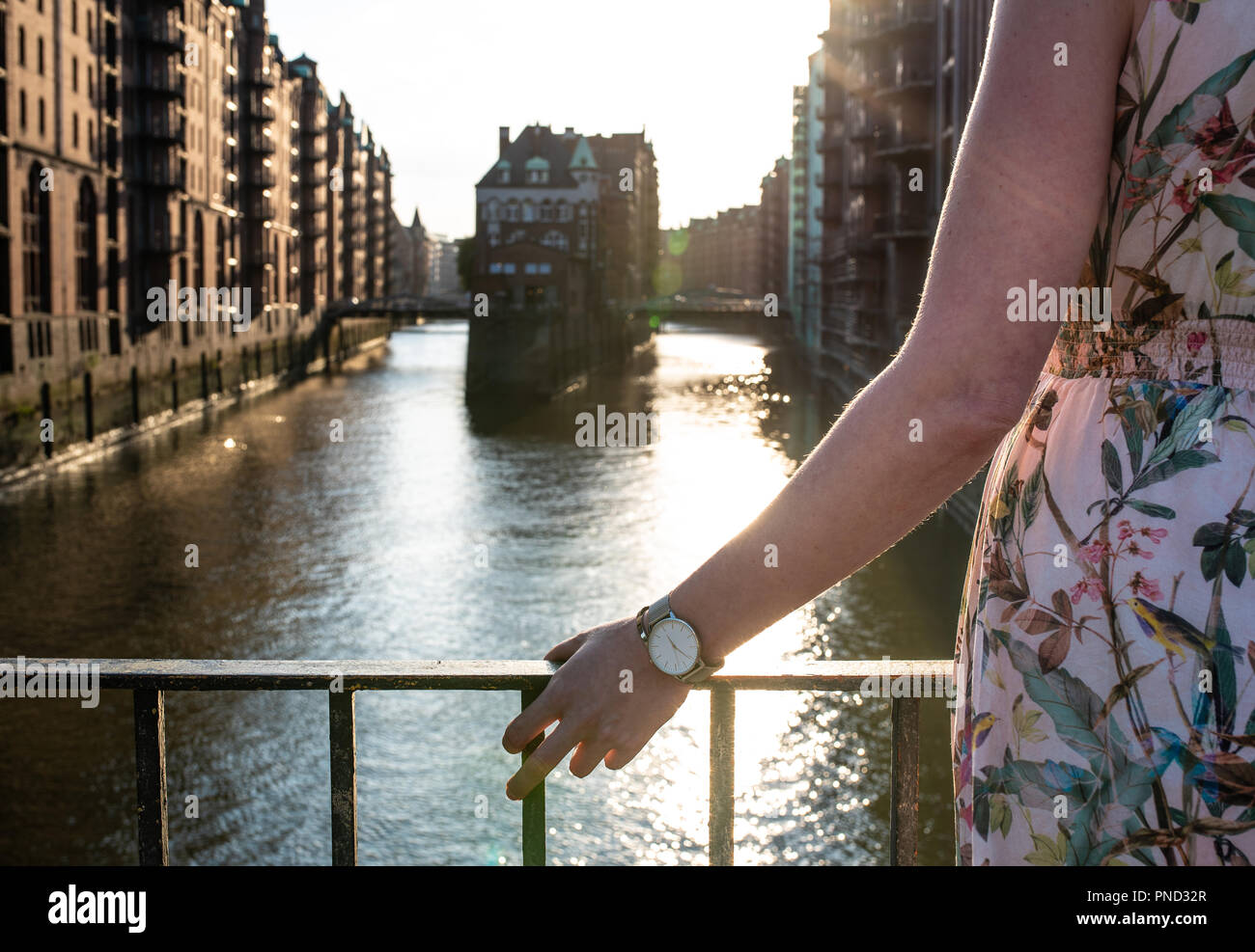 Vista posteriore della donna in appoggio il suo braccio sulla ringhiera del ponte contro canal e di vecchi magazzini in Amburgo Foto Stock