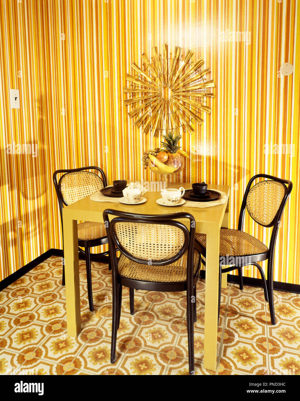Anni Settanta un angolo da pranzo arancio e giallo carta da parati a strisce Arancione marrone tavolo sedie di vimini medaglione a raggiera sulla parete - ki2862 HAR001 HARS in vecchio stile Foto Stock