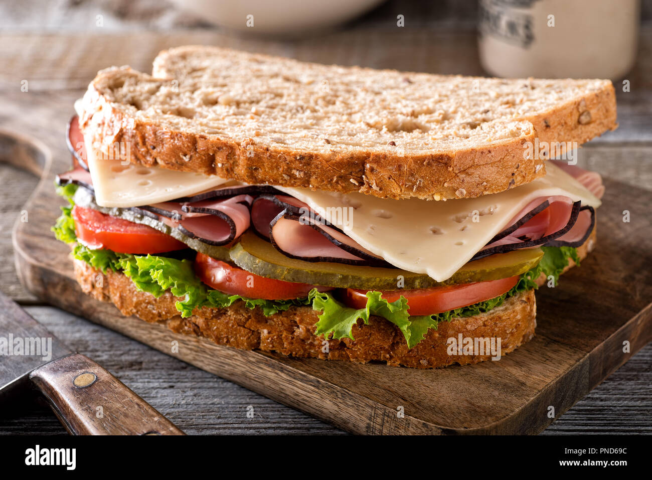 Un delizioso formaggio e prosciutto panino con lattuga, pomodoro e aneto sottaceto su una tavola in legno rustico. Foto Stock