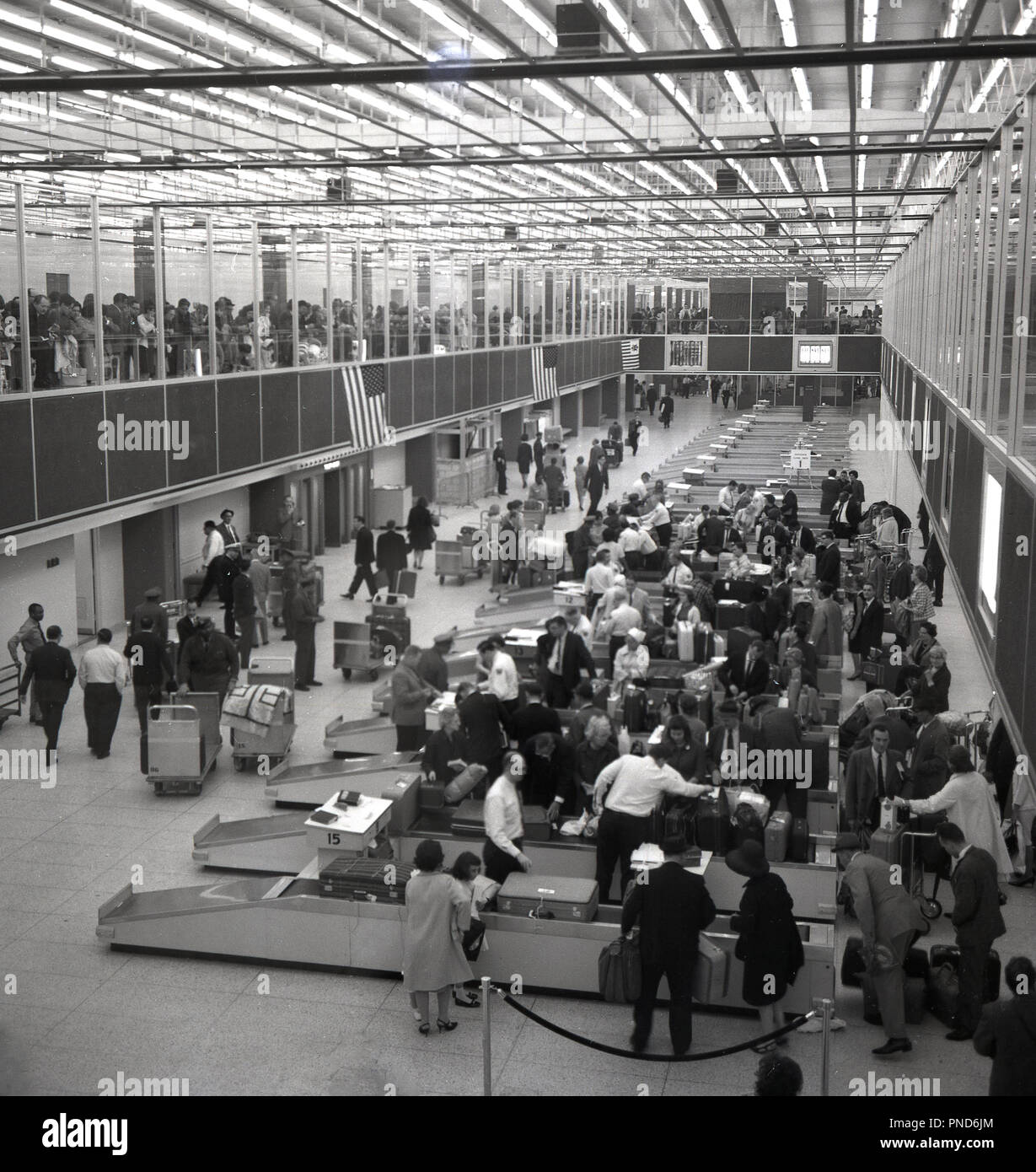 1960, storico, spettatori guardare da un altro livello come i passeggeri del volo per guardare i loro bagagli nella sala bagagli di New York aeroporto internazionale della città o aeroporto di Edoardo Vianello come era comunemente sapere al momento. Successivamente è stato rinominato come JFK in memoria dell'ex presidente degli Stati Uniti. Foto Stock