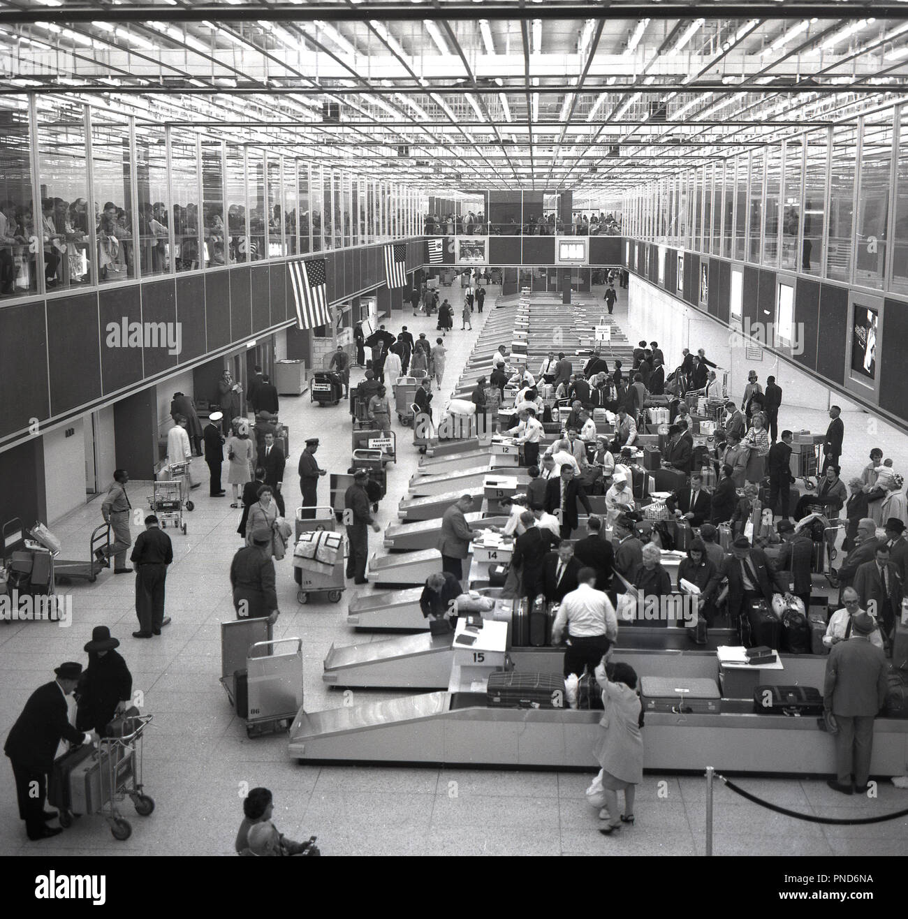 1960, storico, spettatori guardare da un altro livello come i passeggeri del volo per guardare i loro bagagli nella sala bagagli di New York aeroporto internazionale della città o aeroporto di Edoardo Vianello come era comunemente sapere al momento. Successivamente è stato rinominato come JFK in memoria dell'ex presidente degli Stati Uniti. Foto Stock