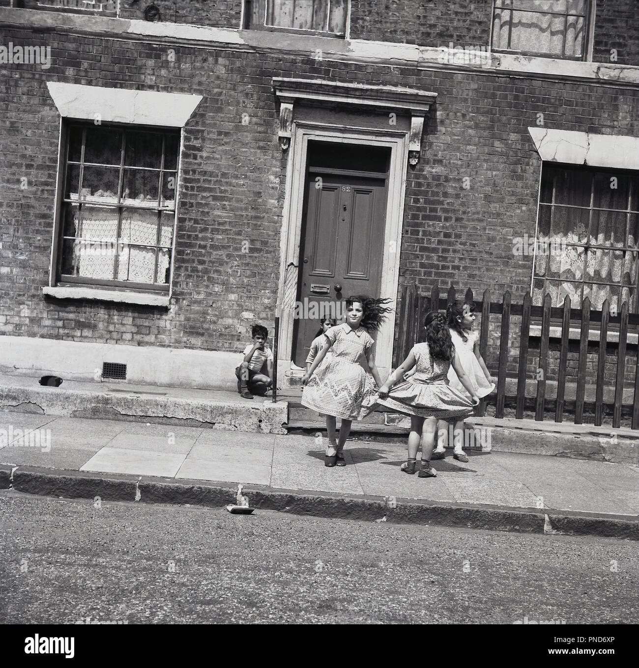 Anni sessanta, storico, giovani ragazze che giocano insieme sul marciapiede esterno a schiera vittoriana alloggiamento in un inner-city Street, Camden, London, England, Foto Stock