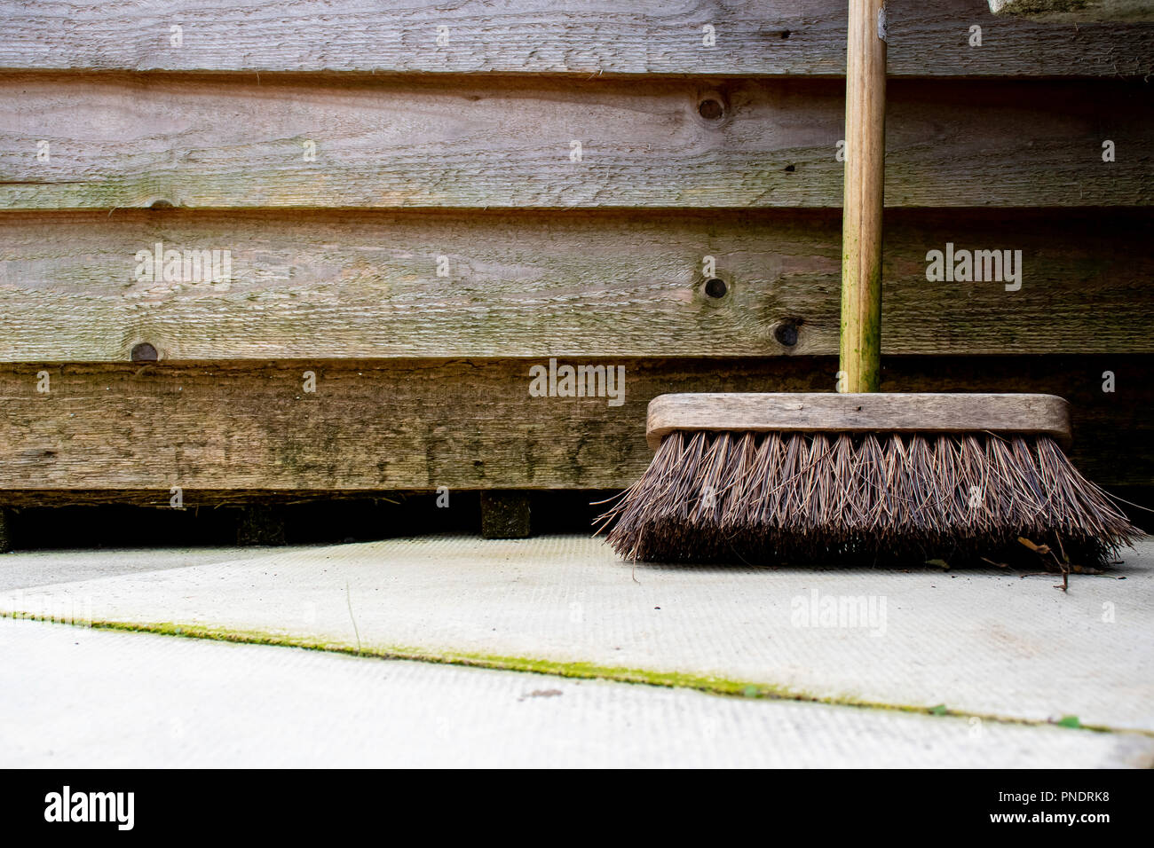 Spazzola giardino appoggiata contro la tettoia in legno sul patio Foto Stock