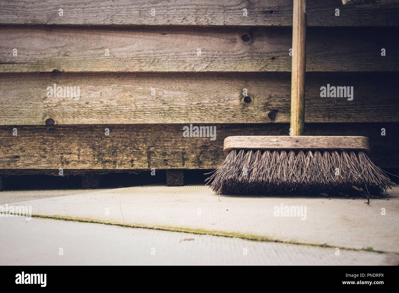 Spazzola giardino appoggiata contro la tettoia in legno sul patio Foto Stock