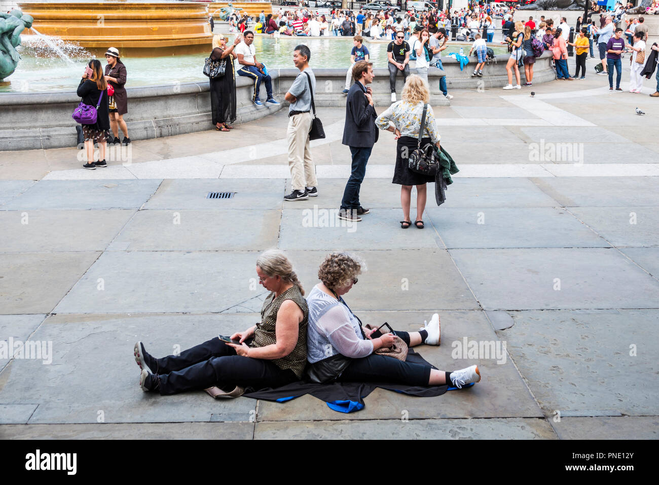 Londra Inghilterra,UK,Trafalgar Square,Public plaza,crowd,donna donne,anziani cittadini,seduta di nuovo a terra su marciapiede,intelligente Foto Stock