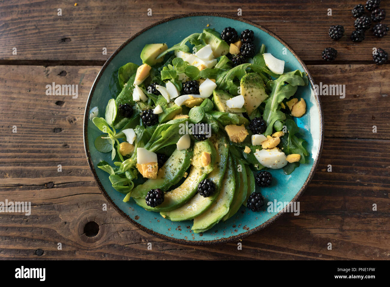 Insalata di avocado con uova, la valeriana, blackberry e rucola su una piastra su un vecchio sfondo di legno Foto Stock