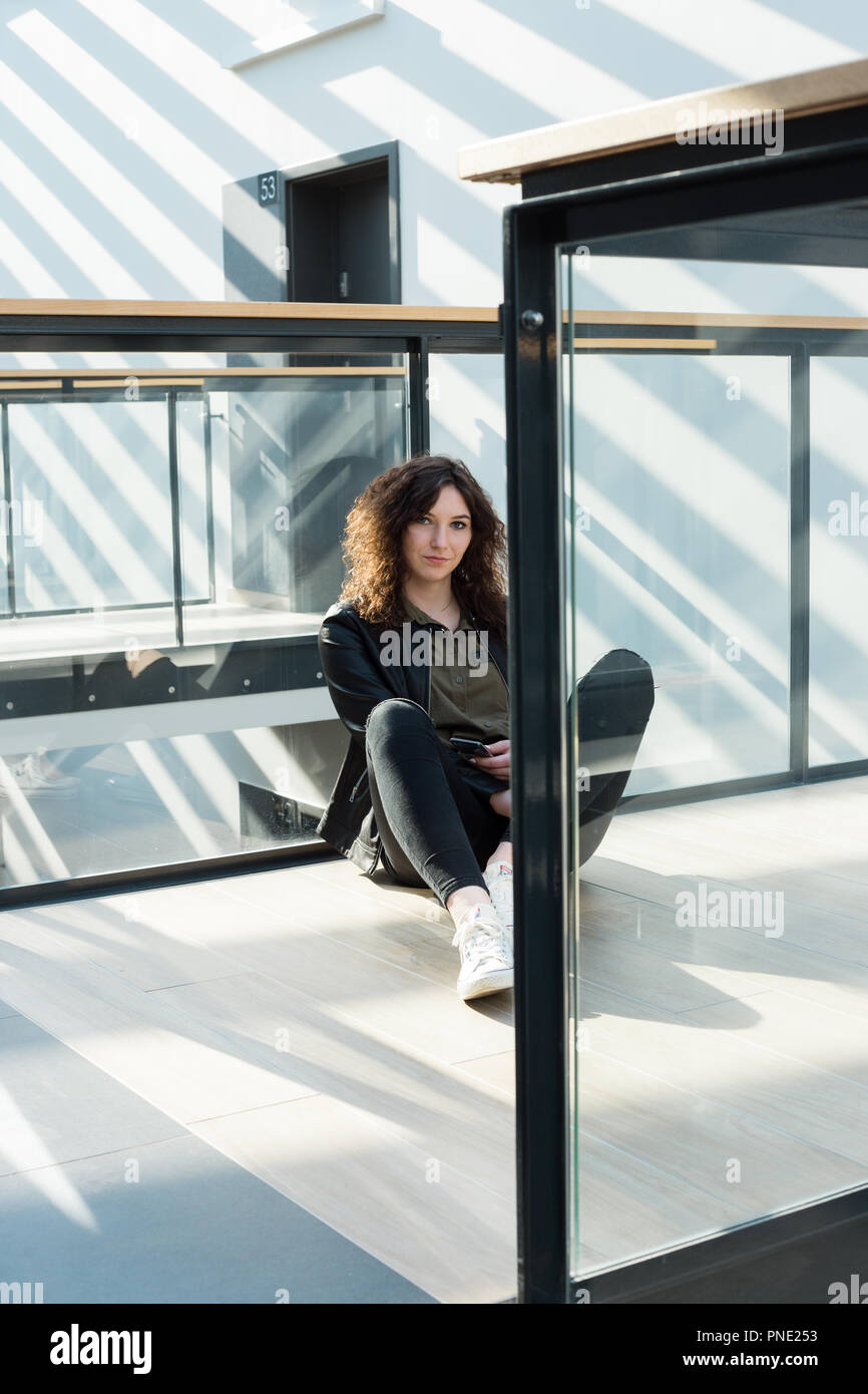 Giovane donna seduta sul pavimento in un ufficio moderno o edificio del campus Foto Stock