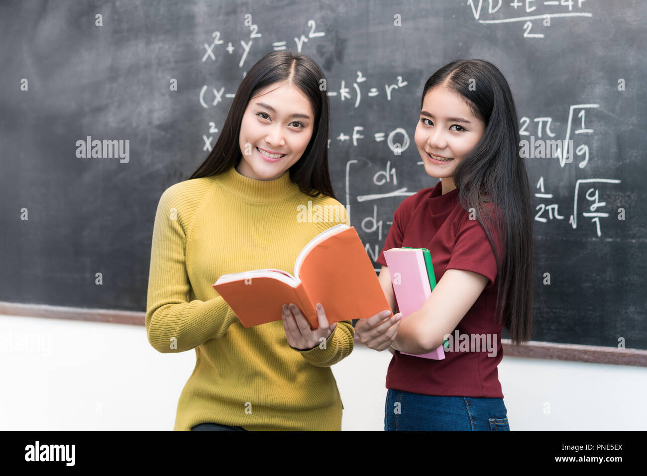 Donna asiatica studente su lavagna holding e la lettura di libri togetherin classroom in università. Il concetto di istruzione. Foto Stock