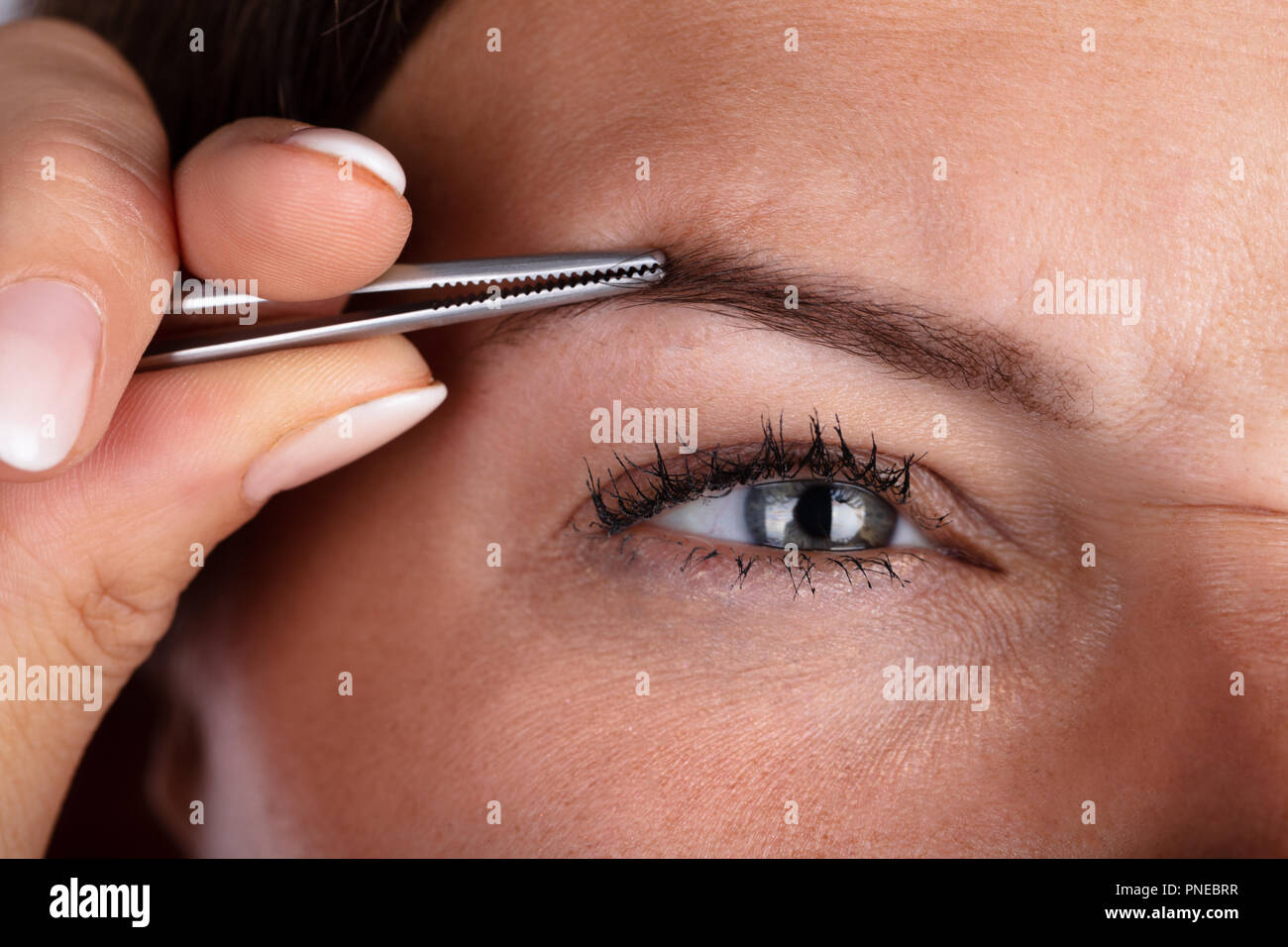 Close-up di una donna di mano spiumatura peli delle sopracciglia con pinzette Foto Stock