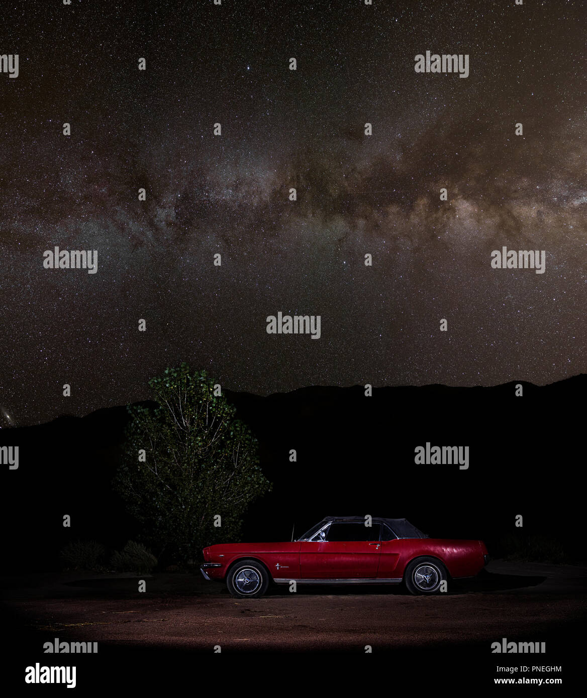 1965 Red Convertibile Ford Mustang fotografato fianco a fianco accanto ad un albero sotto la Milky Way Galaxy Foto Stock