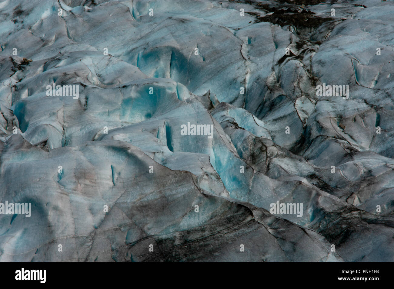 Una vista ravvicinata della superficie ghiacciata aspra e azzurra di un ghiacciaio norvegese con fessure e striature scure di detriti. Foto Stock