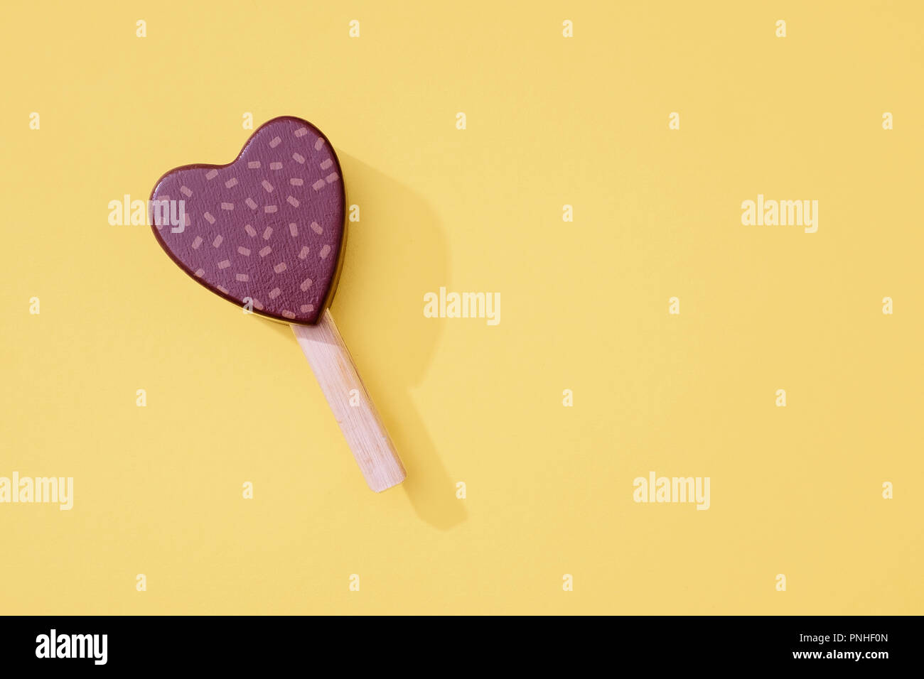 Giocattolo di legno cuore di cioccolato ice lollipop ghiaccioli con spruzza su sfondo giallo con bastone di legno e lo spazio per la copia e il testo. Foto Stock