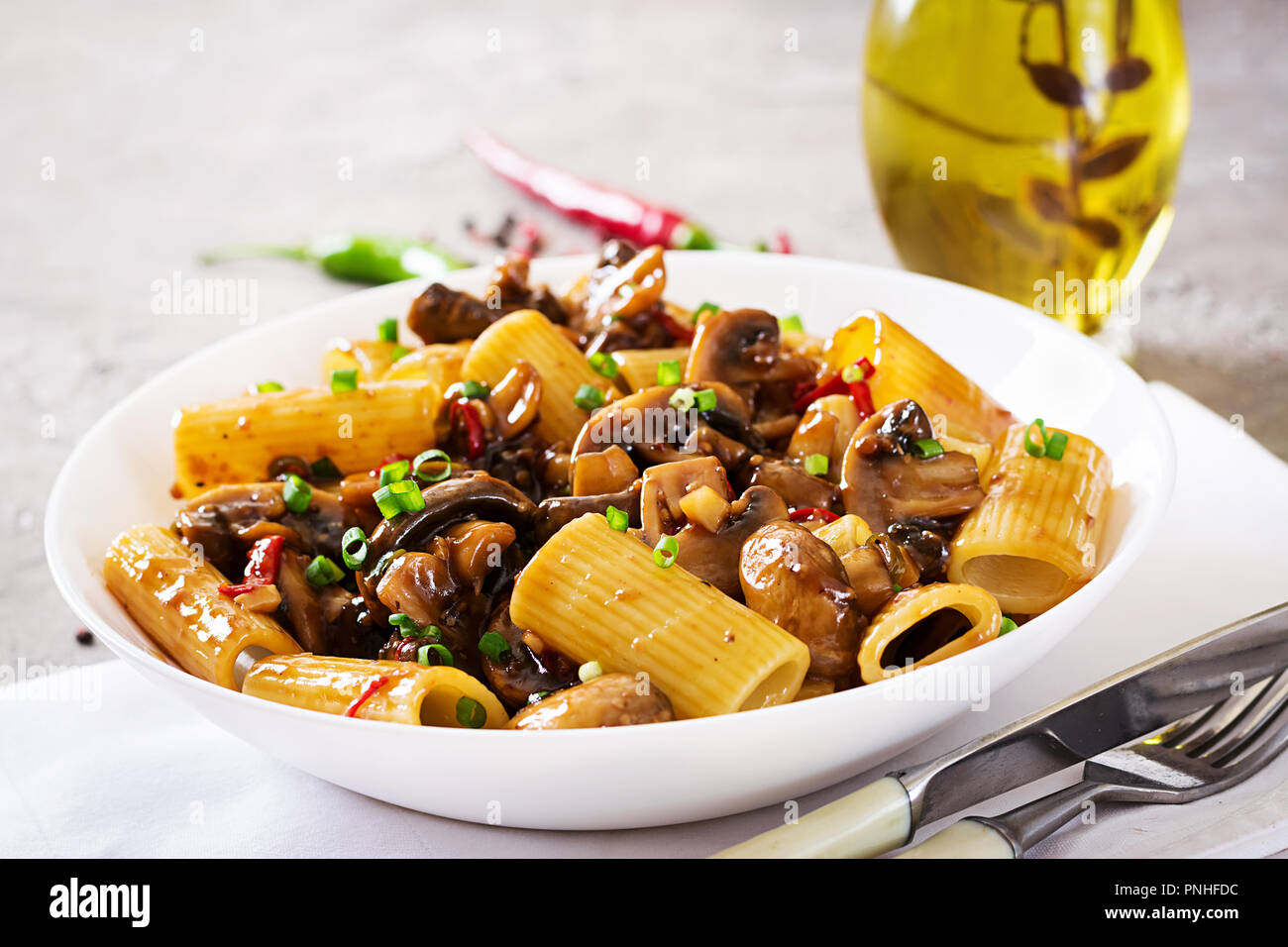Pasta Vegetariana rigatoni con funghi e peperoncino in vaso bianco sulla tabella grigia. Cibo vegan. Foto Stock