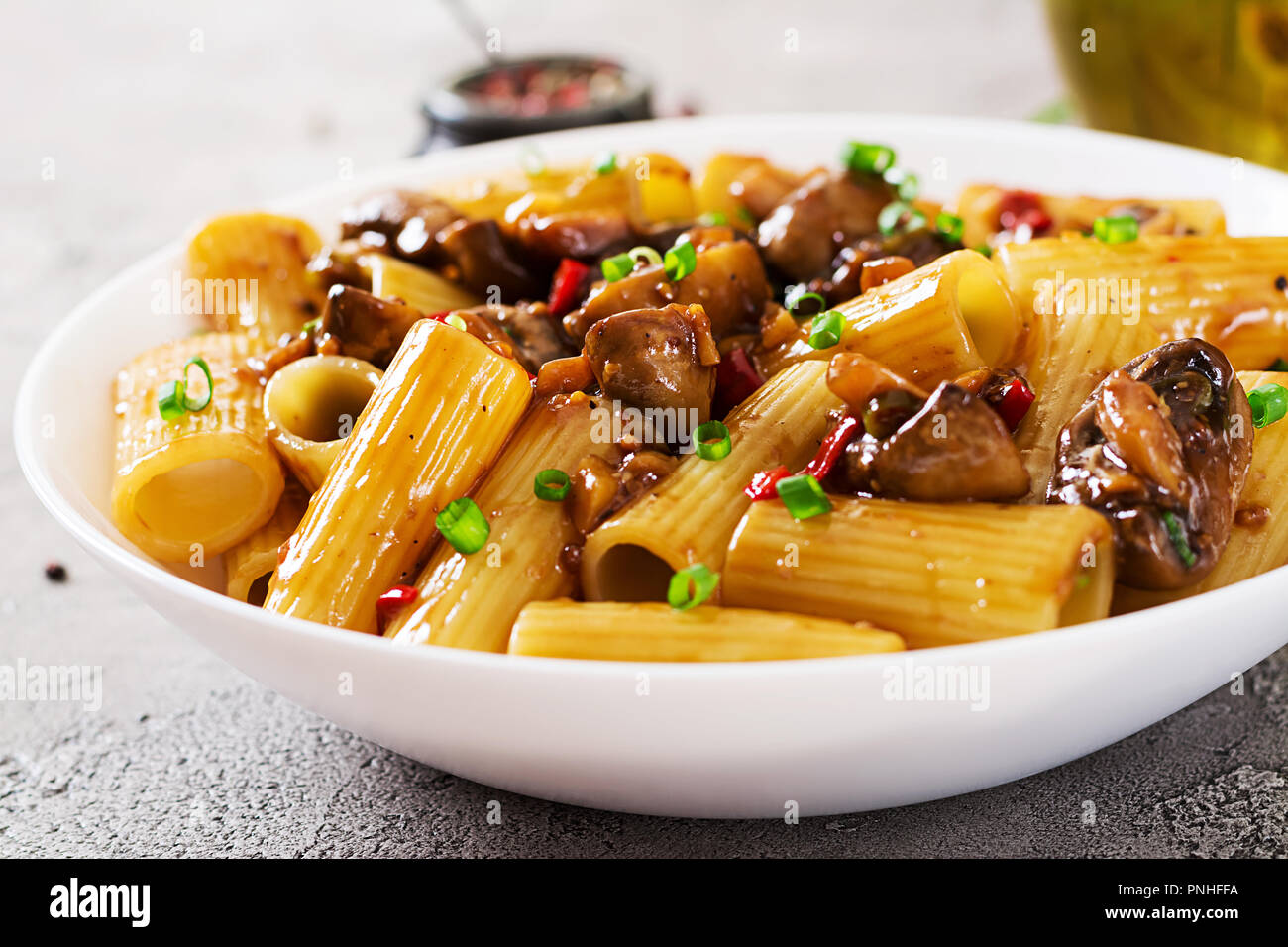 Pasta Vegetariana rigatoni con funghi e peperoncino in vaso bianco sulla tabella grigia. Cibo vegan. Foto Stock