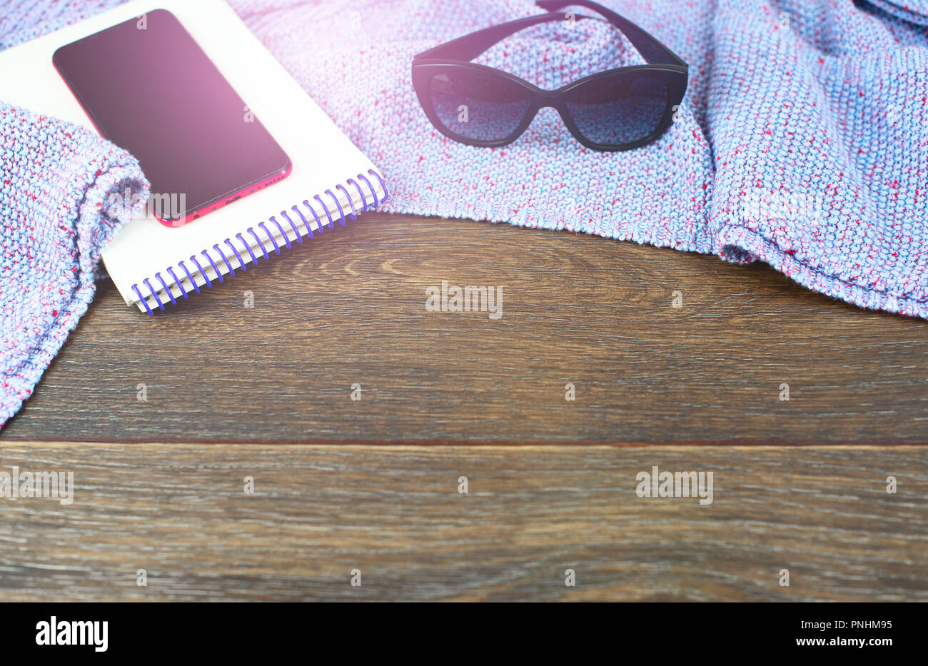 Spazio vuoto sul desktop mobile phone gadget Notepad occhiali da sole. Il vecchio legno naturale sfondo squallido coperta di maglia plaid color porpora sole g Foto Stock