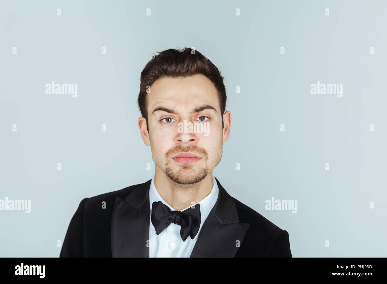 Ritratto di un giovane uomo bello in uno smoking, seriamente guardando la telecamera, contro pl​ain di sfondo per studio. Foto Stock
