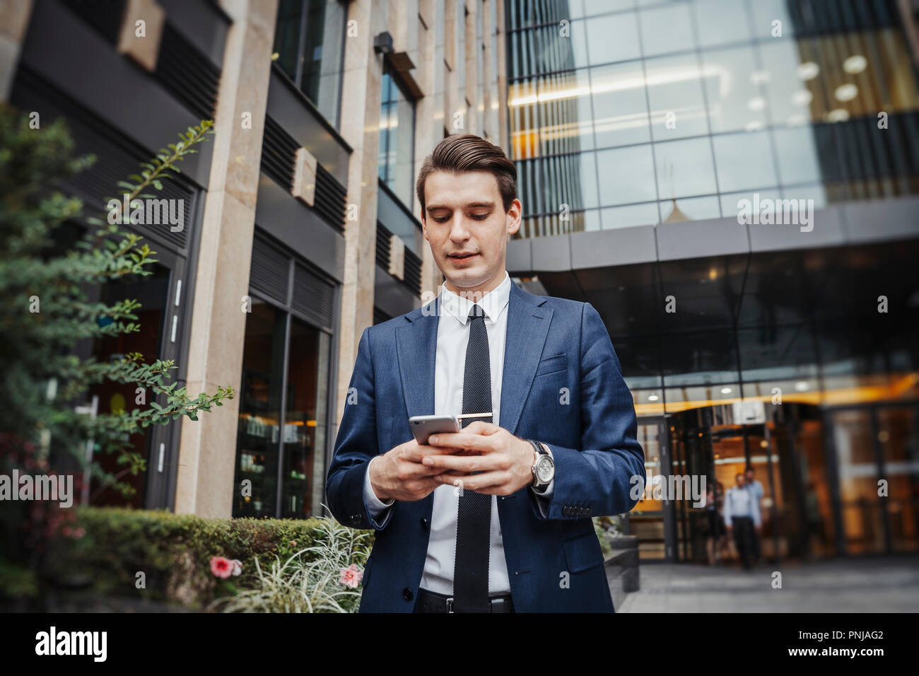 Close up di imprenditore accanto al grattacielo guardando lo schermo del telefono cellulare. Foto Stock
