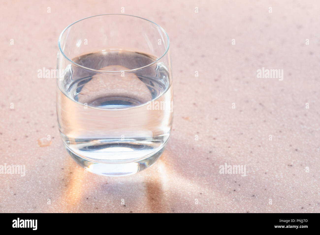 Parzialmente riempita di vetro con acqua chiara sulla scheda rosa Foto Stock