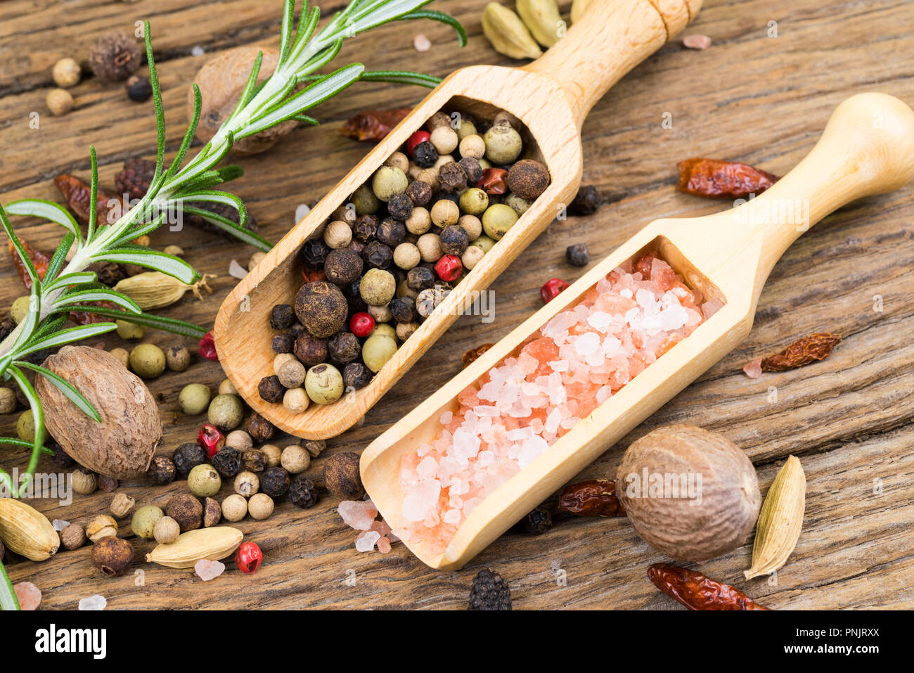 Primo piano di pepe colorato e rosa con cristalli di sale in piccole casette di legno spice scoop su legno rustico sfondo con un rametto di rosmarino in backgroun Foto Stock