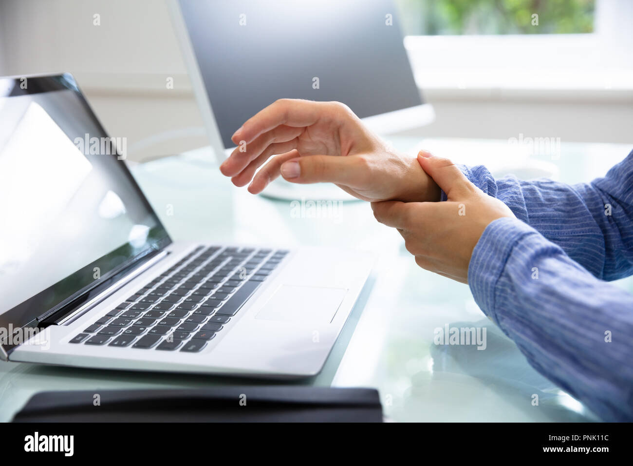 Close-up di una imprenditrice la mano che tiene la sua dolorosa polso con laptop sulla scrivania Foto Stock