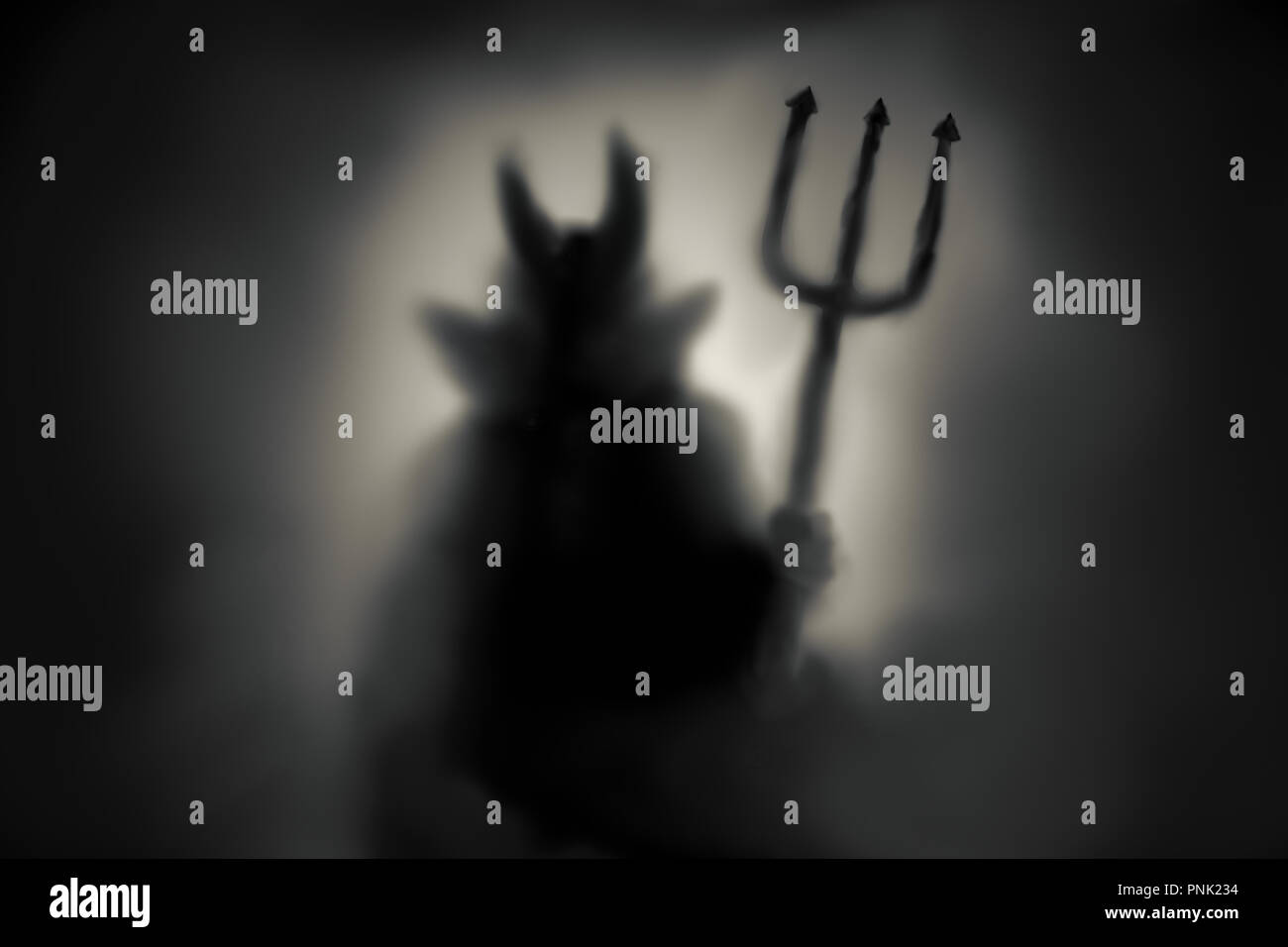 Creepy diavolo silhouette dietro un vetro congelato e nella nebbia con retroilluminato. Foto Stock