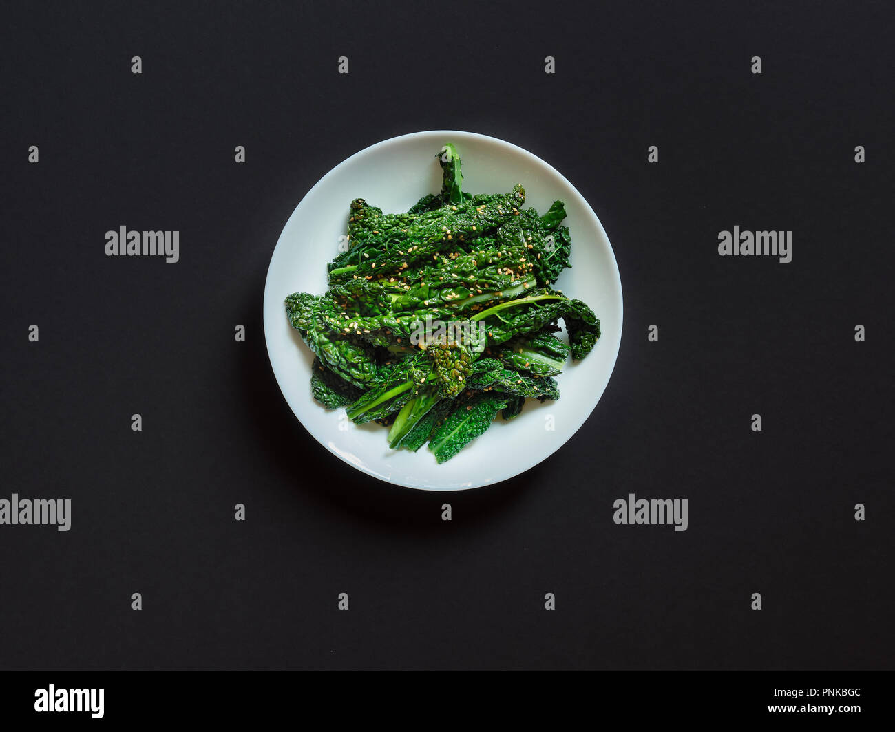 Vista dall'alto di un piatto di cavolo cotto con seasame semi e ail su uno sfondo nero in studio Foto Stock
