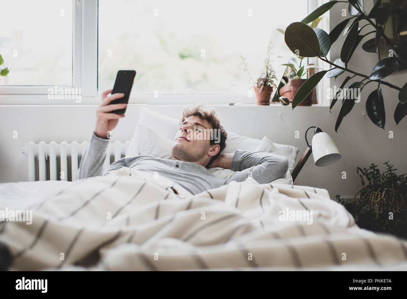 Giovani maschi adulti il controllo dello smartphone come egli si sveglia al mattino Foto Stock