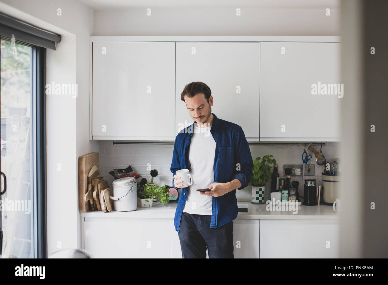 Maschio adulto controllo smartphone in cucina con la tazza di caffè Foto Stock