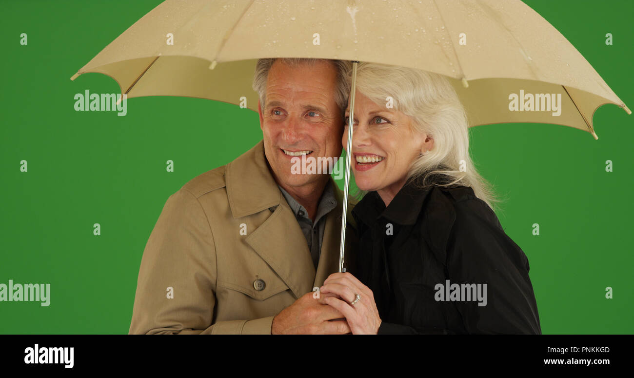Felice coppia di anziani in piedi sotto la pioggia con un ombrello su schermo verde Foto Stock