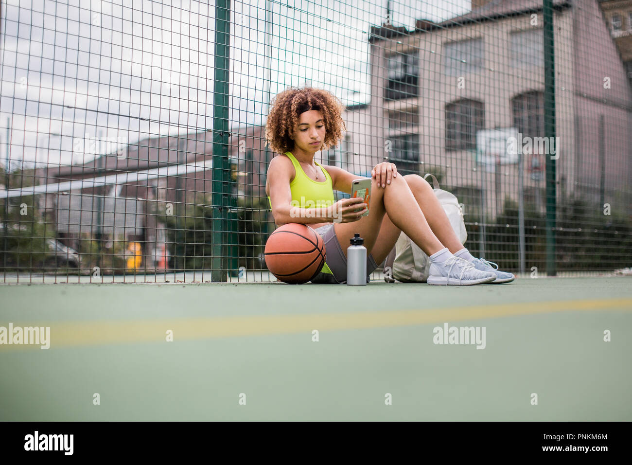 Giovane femmina adulta su un campo da basket utilizza lo smartphone Foto Stock