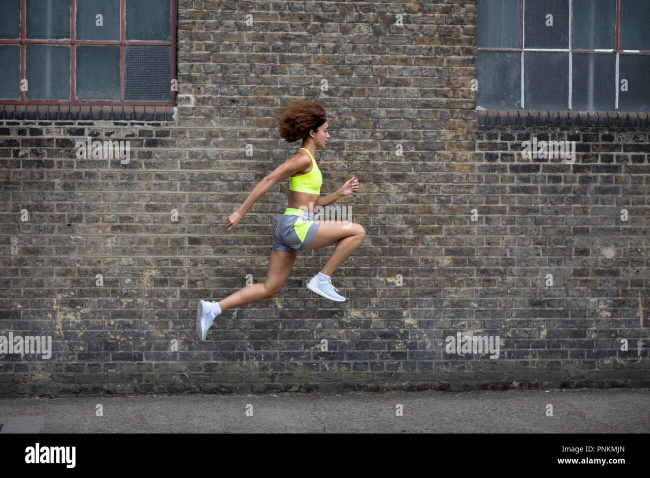 Giovane femmina adulta salta in aria con un muro di mattoni sfondo Foto Stock