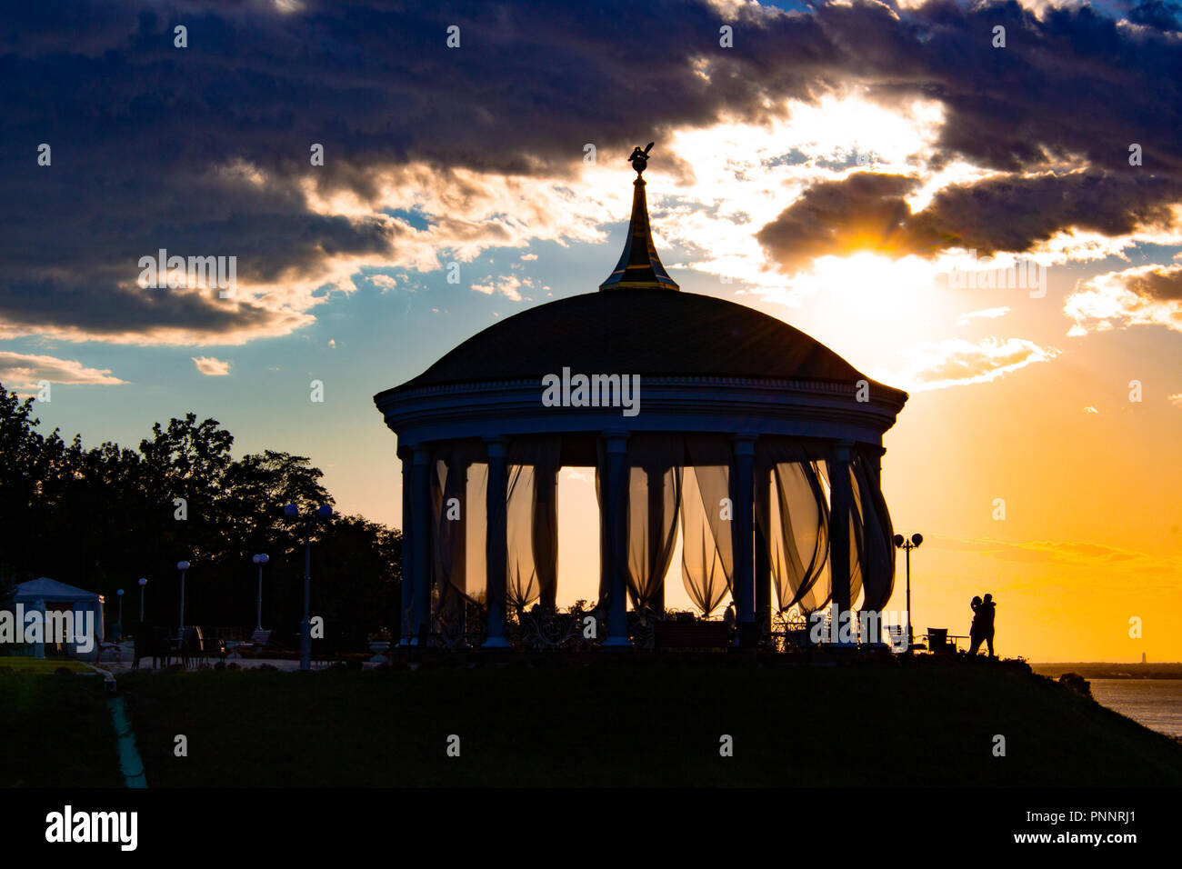 Un giovane in amore baci e abbracci accanto a un romantico gazebo contro il tramonto Foto Stock