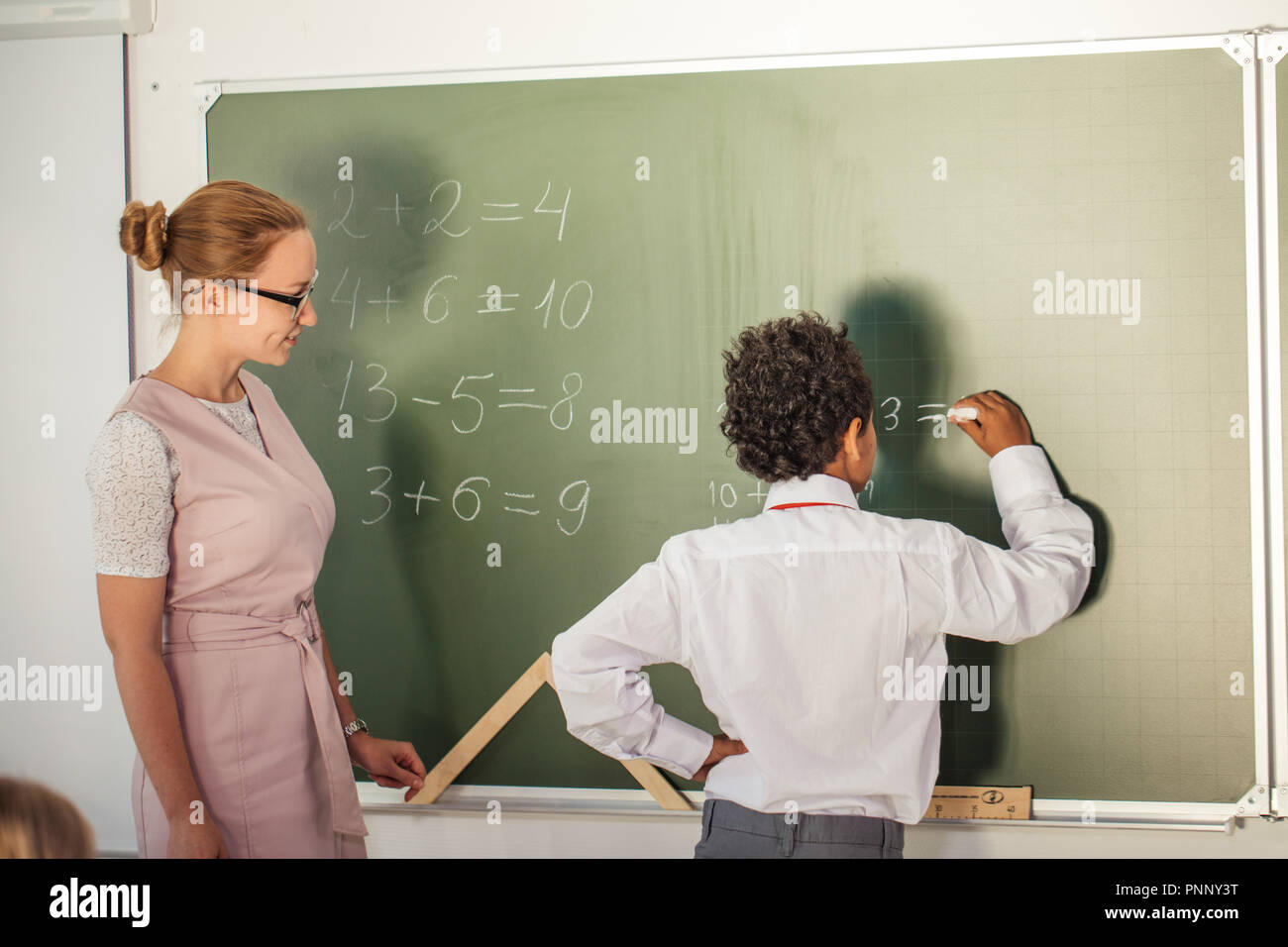 Ragazzo la risoluzione di addizione e sottrazione a bordo. scolaro iscritto soluzione di operazione matematica Foto Stock