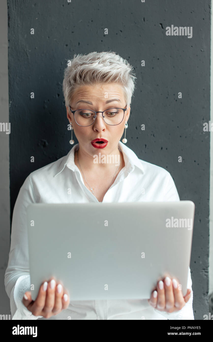 La donna ha sorpreso la lettura di informazioni inaspettata nel computer portatile con la bocca aperta e gli occhi di rigonfiamento Foto Stock