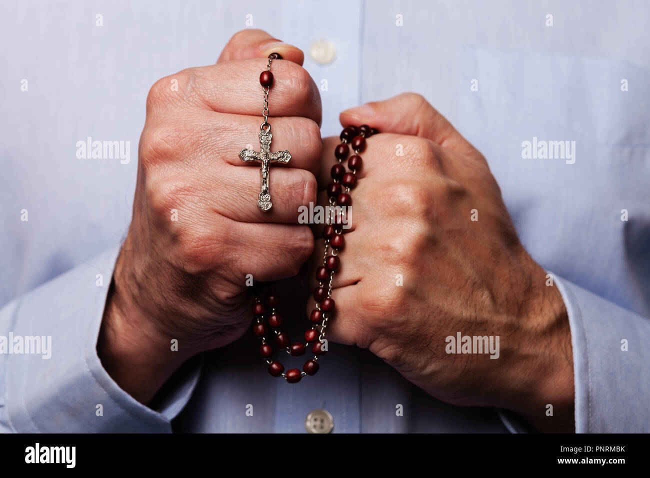Mani maschio pregando tenendo un rosario perline con Gesù Cristo in croce o Crocifisso su sfondo nero. Uomo maturo con cristiana religiosa cattolica Foto Stock