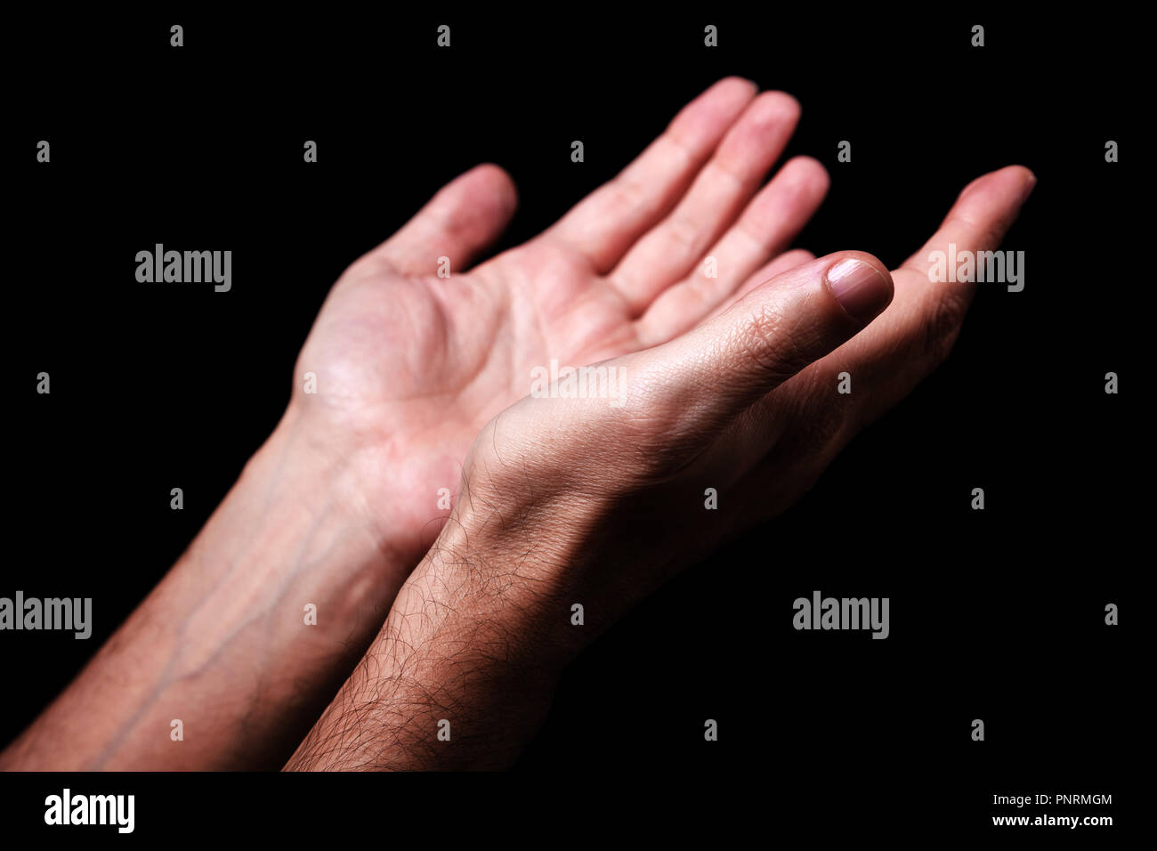 Maschio pregando le mani con i palmi rivolti verso l'alto braccia tese. Sfondo nero. Close up man mano. Concetto di preghiera e di fede e di religione, religiosi, di culto Foto Stock