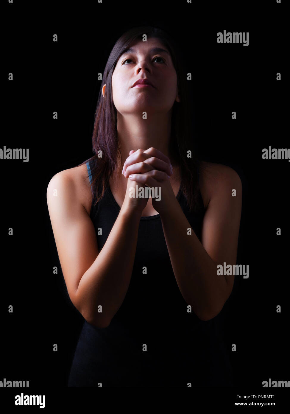 Fedeli donna orante, mani piegate in adorazione a Dio con cercando in fervore religioso, su uno sfondo nero. Concetto di religione, fede, la preghiera Foto Stock