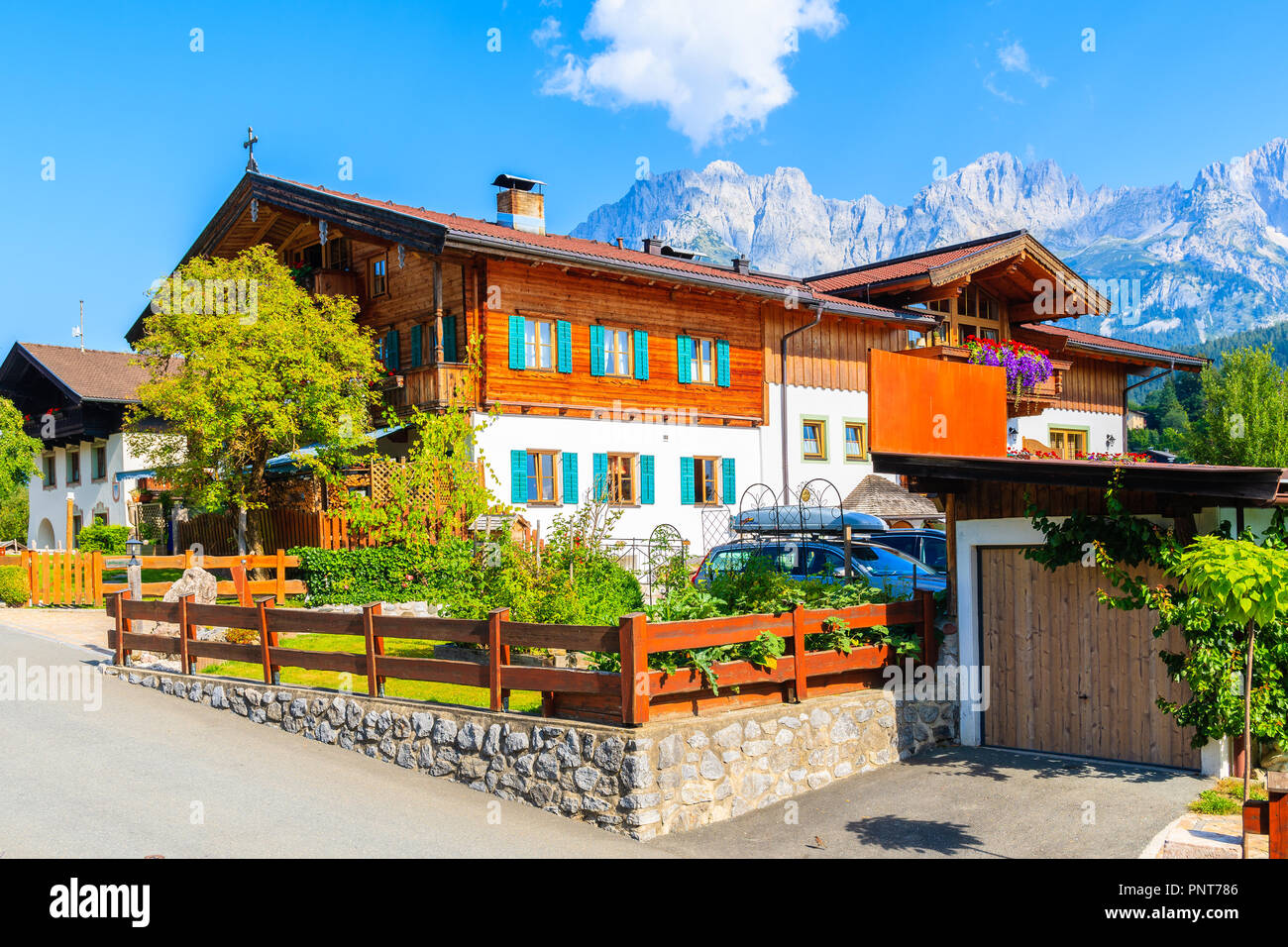 Tradizionale alpino in legno casa decorata con fiori sul prato verde a Going am Wilden Kaiser villaggio montano su soleggiate giornate estive, Tirolo, Austria Foto Stock