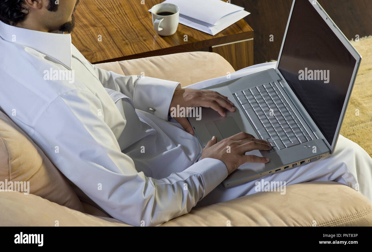 Uomo Mideastern utilizzando portatile a casa con una tazza di caffè e documenti sul lato tavolo Foto Stock