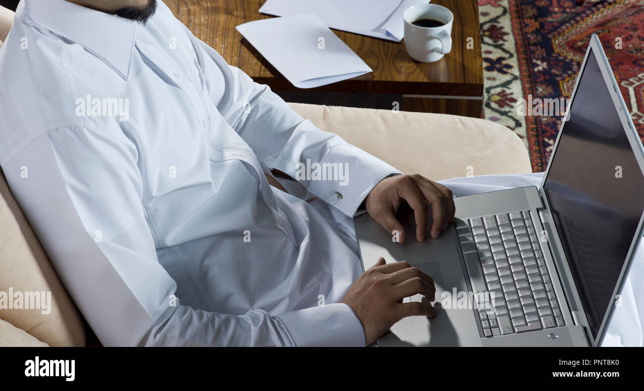 Uomo Mideastern utilizzando portatile a casa con una tazza di caffè e documenti sul lato tavolo Foto Stock