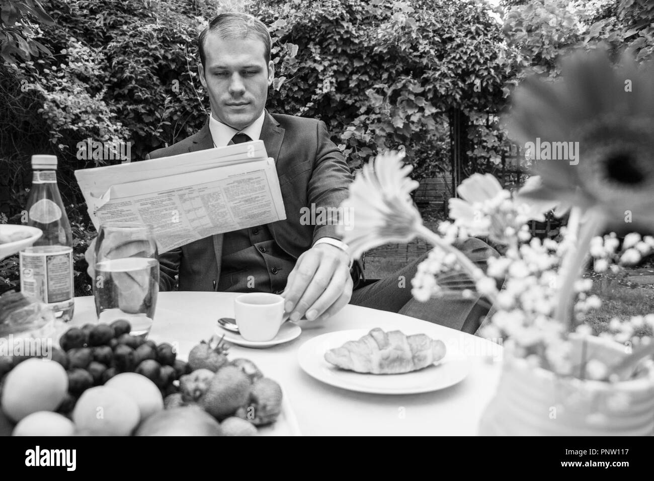 Bel uomo vestito di vintage abito classico di bere caffè al tavolo durante la lettura del giornale Foto Stock