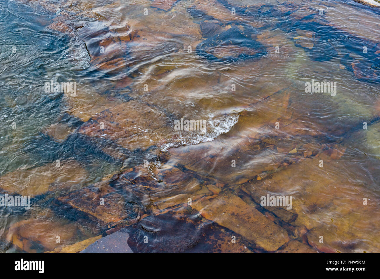 Cancellare l'acqua di un fiume che scorre su rocce che vi permette di vedere sotto per le rocce Foto Stock